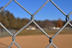 Close-up of a baseball bat leaning against a chain-link fence with a blurred stadium background.