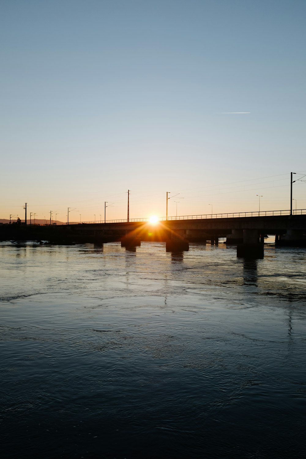 the sun is setting on a bridge over a body of water