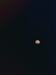 A small, bright celestial body, possibly the moon, appears against a vast, dark sky. The surrounding darkness is dotted with faint stars, contributing to a serene and vast atmosphere.
