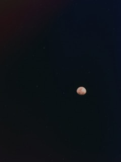 A small, bright celestial body, possibly the moon, appears against a vast, dark sky. The surrounding darkness is dotted with faint stars, contributing to a serene and vast atmosphere.