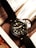 A wristwatch with a black leather strap and a dark dial is placed on top of a magazine or catalog featuring a car image. The watch has bold hour markers and numerals on the bezel, with what appears to be hands displaying the time.