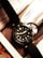 A wristwatch with a black leather strap and a dark dial is placed on top of a magazine or catalog featuring a car image. The watch has bold hour markers and numerals on the bezel, with what appears to be hands displaying the time.