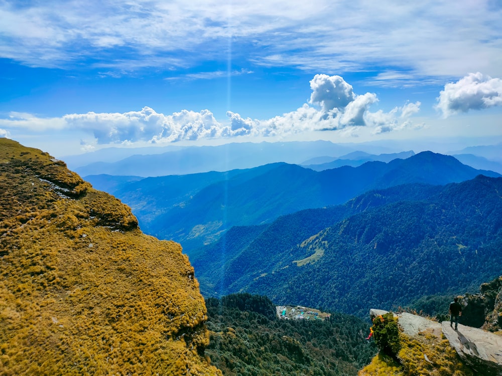 a man standing on top of a mountain next to a lush green hillside