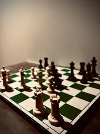 A close-up view of a chessboard with the chess pieces set up for a game. The board is arranged with ivory-colored pieces on one side and darker pieces on the opposite side. The lighting creates a dramatic shadow effect, emphasizing the intricate details of the pieces and the squares on the board.