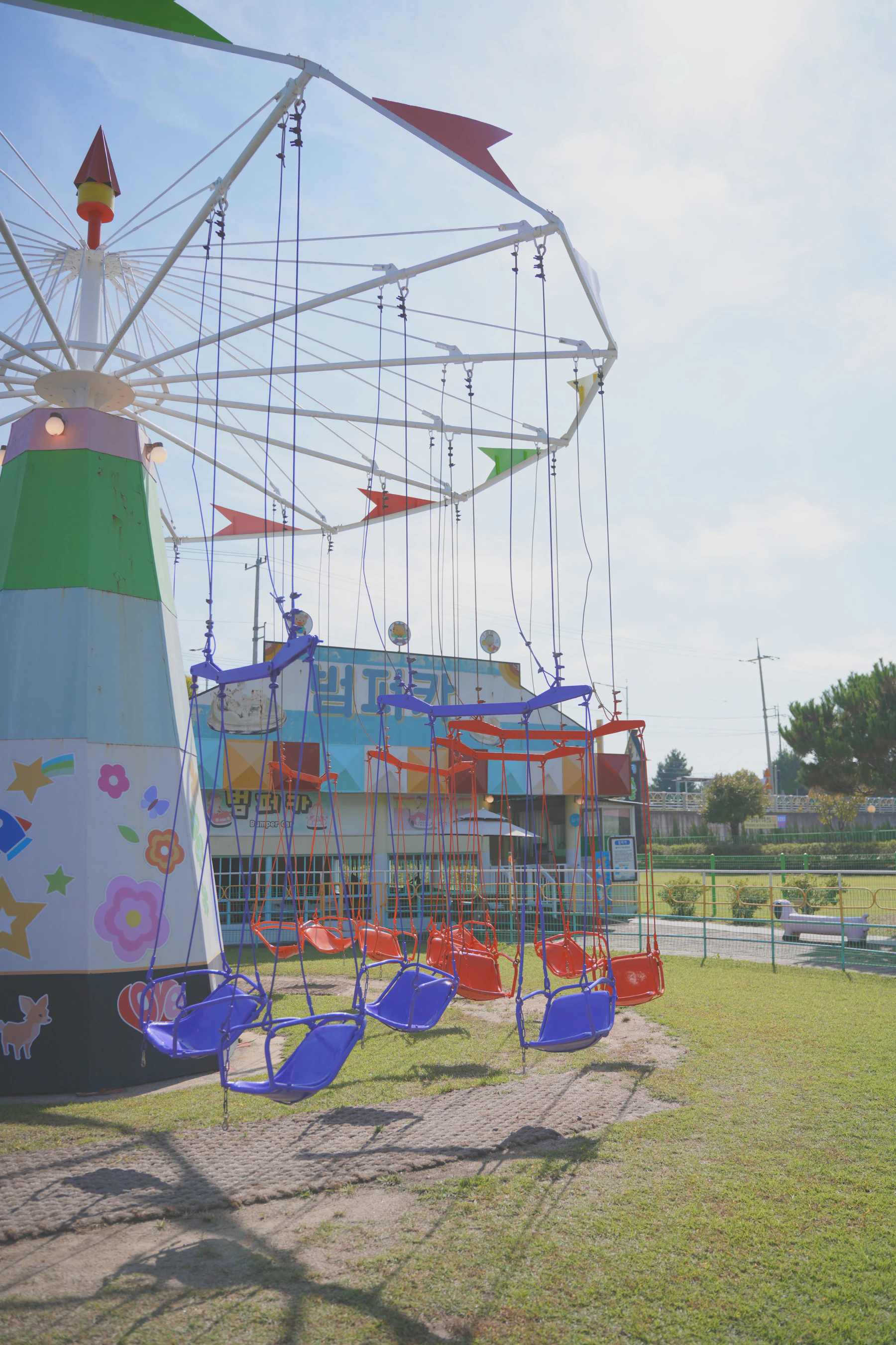 A chair swing ride standing still at a small amusement park, its red and blue seats hanging on chains under a frame strung with pennants