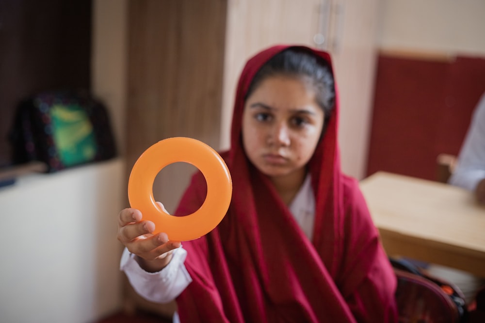 a woman in a red shawl holding an orange object