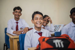 A group of enthusiastic Indonesian students studying together with books and laptops in a bright classroom.