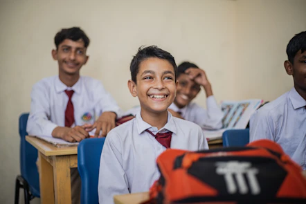 A joyful group of children studying together in a bright classroom filled with books and digital devices.