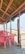 A rustic beachside setup with a wooden structure featuring a thatched roof, overlooking the sea. Inside the structure, several red plastic chairs surround a table. The view extends out to the sandy beach and the ocean, creating a tranquil and scenic atmosphere.