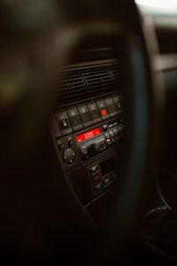 The interior of a car featuring a close-up of the dashboard and control panel. The focus is on the center console where the temperature and audio controls are located. The display shows a digital radio station reading with the text 'KISS'. The surrounding area includes dials, buttons, and vents.