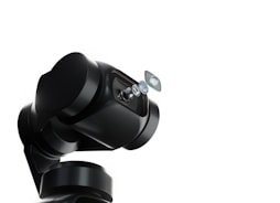 A robotic arm with a sleek, black design holds a series of lenses that appear to be suspended in mid-air. The background is a stark white, emphasizing the mechanical and sophisticated nature of the robotic technology.