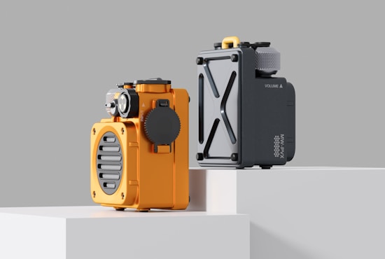 Two modern and compact devices with a retro design placed on elevated blocks. The left device is orange with a circular grille and various dials; the right device is gray with a minimalist design, featuring a prominent X-shaped detail.