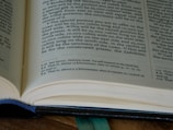 An open book with printed text, including a section of text and footnotes. The pages are light-colored and the text is in a dark font. The book is partially in focus, emphasizing the text at the center.