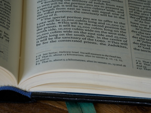An open book with printed text, including a section of text and footnotes. The pages are light-colored and the text is in a dark font. The book is partially in focus, emphasizing the text at the center.