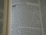 A close-up of an open book displaying a page with text. The layout is divided into sections with bold headings and numbered lists. The font is clear, and the lines of text are closely spaced. The lighting highlights the text, making it easy to read.