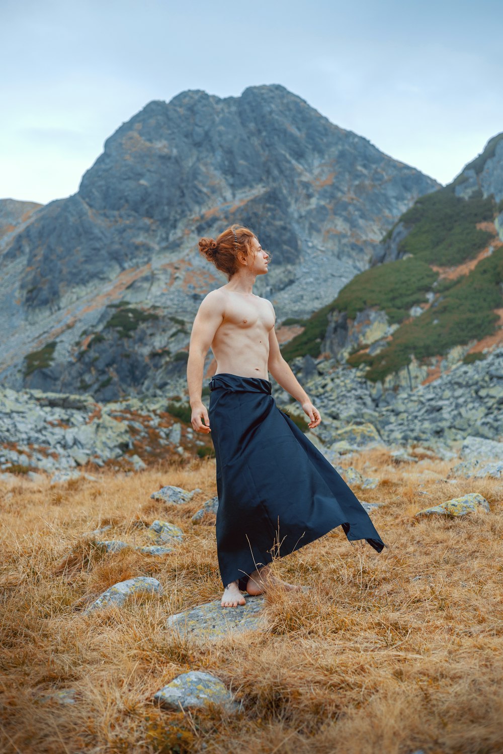 a shirtless man in a long skirt standing in a field