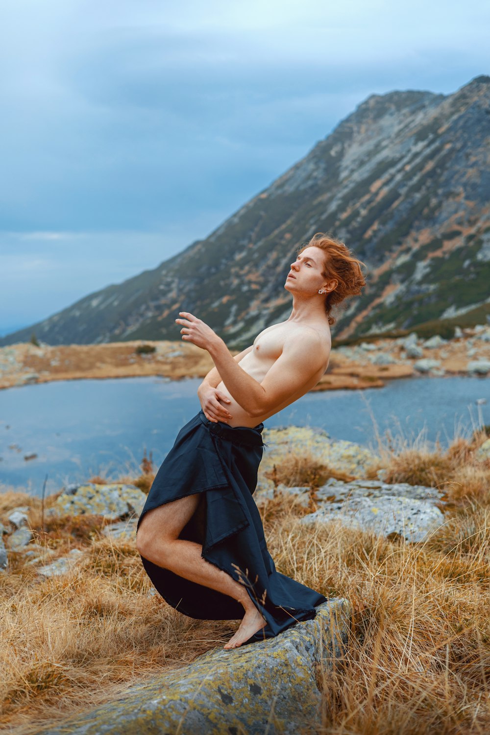 a shirtless man standing on a rock near a body of water