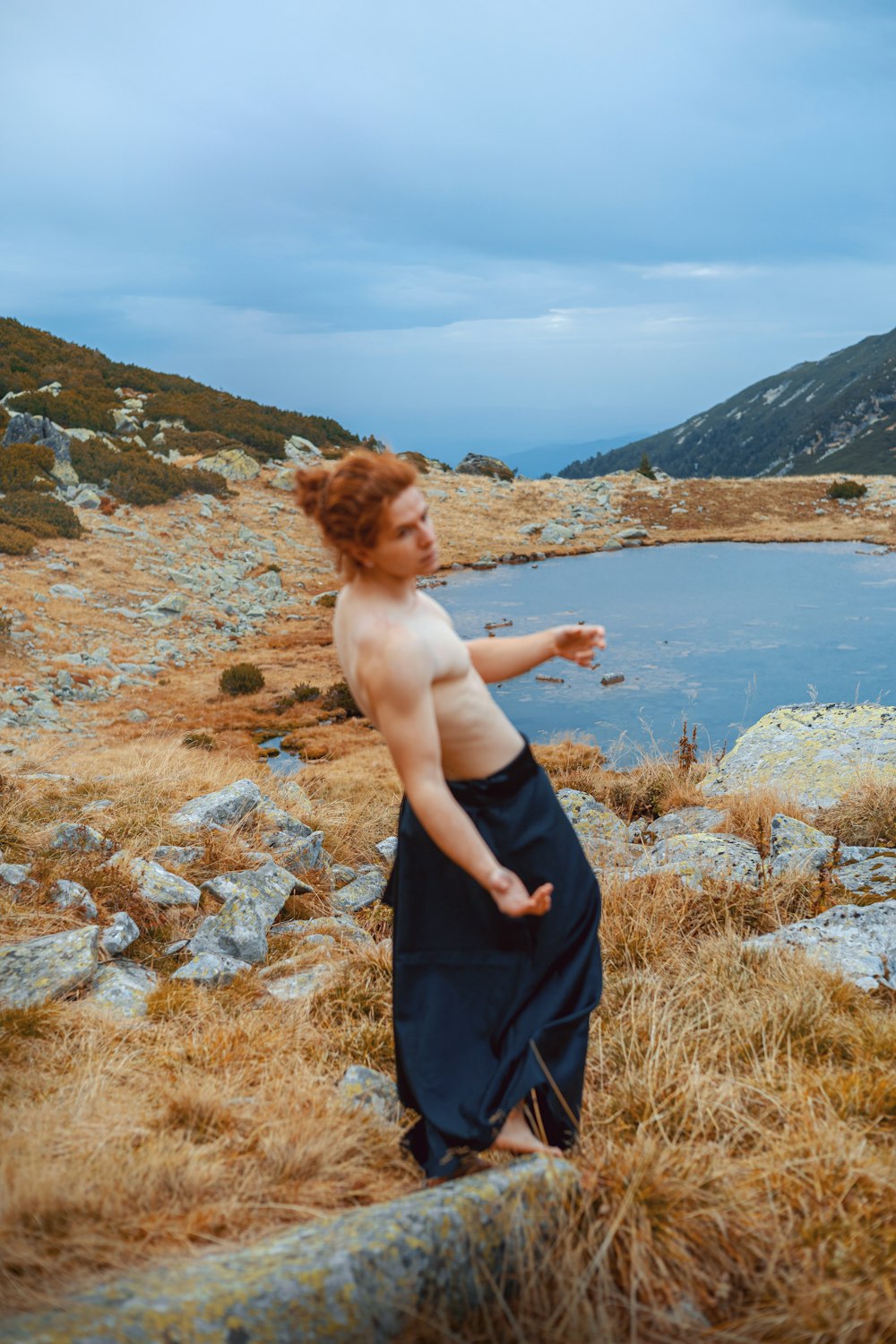 a shirtless man standing on top of a hill next to a body of water