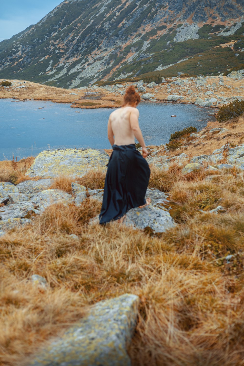 a woman standing on a rocky hillside next to a body of water