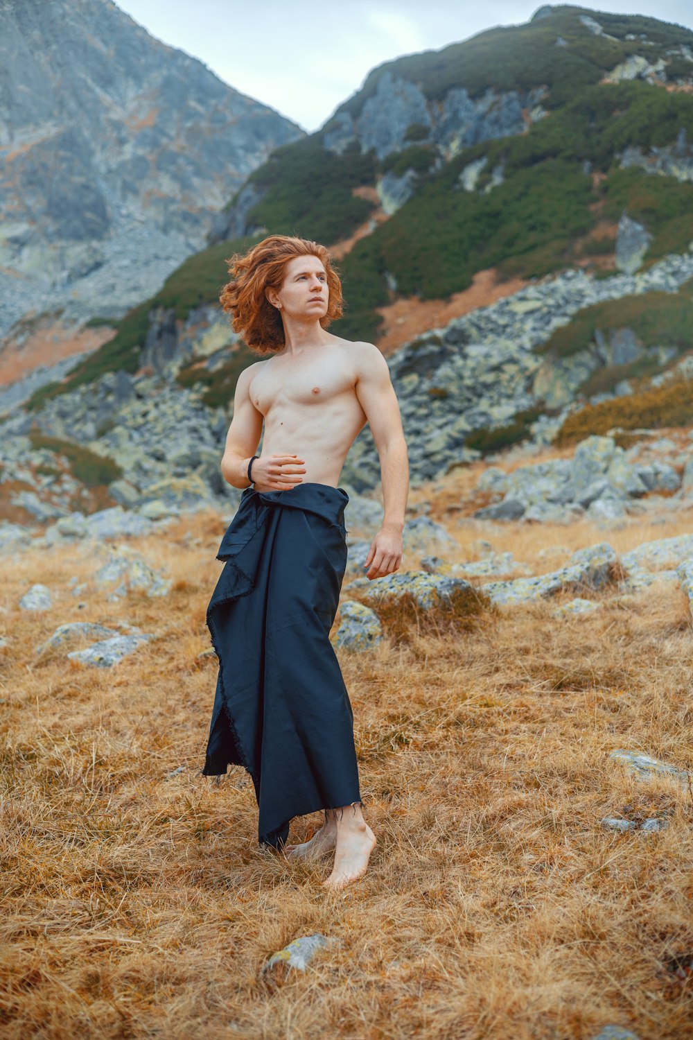 a shirtless man standing in a field with a mountain in the background