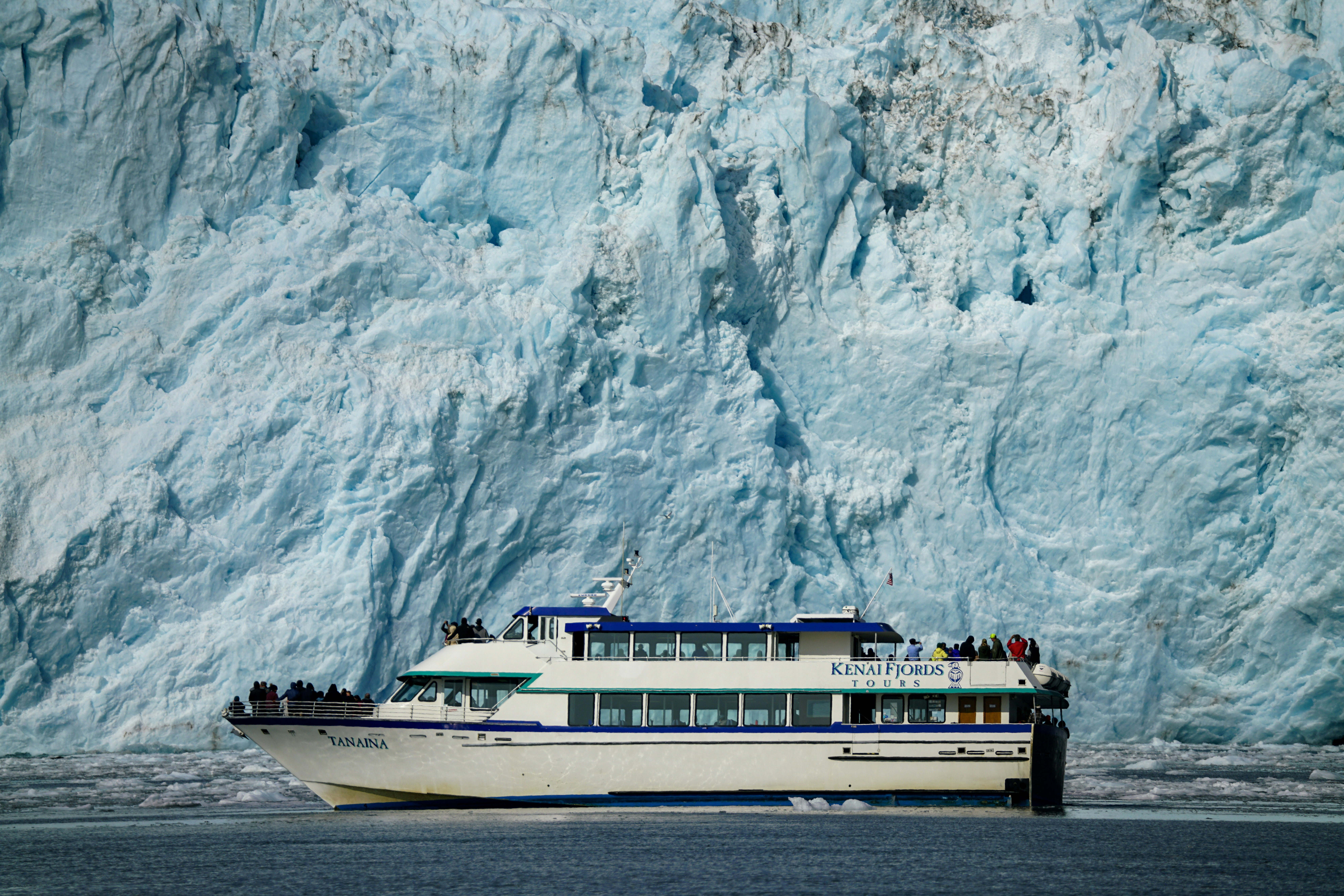 a boat in front of a large glacier wall