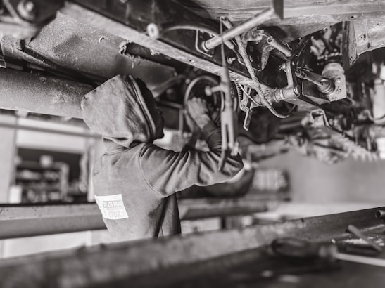 Mechanic inspecting the undercarriage of a large commercial truck in a workshop.