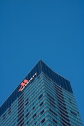 A tall, modern skyscraper with a glass facade dominates the scene, reflecting the clear blue sky. The building features the logo and name of a well-known hotel chain near the top, highlighting its corporate identity.
