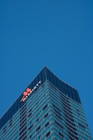A tall, modern skyscraper with a glass facade dominates the scene, reflecting the clear blue sky. The building features the logo and name of a well-known hotel chain near the top, highlighting its corporate identity.