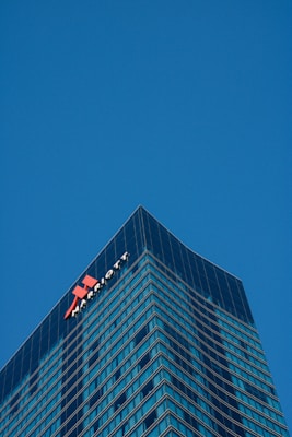 A tall, modern skyscraper with a glass facade dominates the scene, reflecting the clear blue sky. The building features the logo and name of a well-known hotel chain near the top, highlighting its corporate identity.