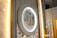 A beautifully decorated wall featuring a large circular plaque with ornate Arabic calligraphy in gold, surrounded by soft, ambient lighting. The background includes intricate white lattice patterns and vertical lines, creating an elegant and sophisticated atmosphere.