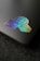 A holographic sticker placed on a sleek, dark surface. The sticker features geometric shapes including a globe, lines, and a diamond pattern, exhibiting a vibrant gradient effect.