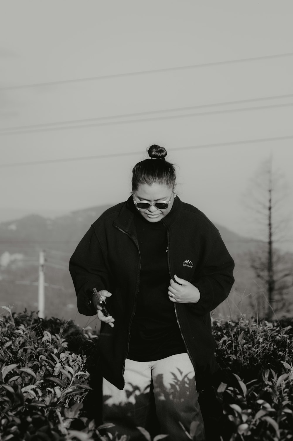 a woman in a black jacket and sunglasses walking through a field