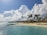 A breathtaking view of a tropical beach with clear blue waters and palm trees swaying.