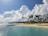A breathtaking view of a tropical beach with clear blue waters and palm trees swaying.