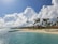 A scenic view of a tropical beach with clear blue water and palm trees swaying in the breeze.