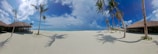 A panoramic view of a white sandy beach framed by lush green palm trees under a deep blue sky in Guadeloupe.