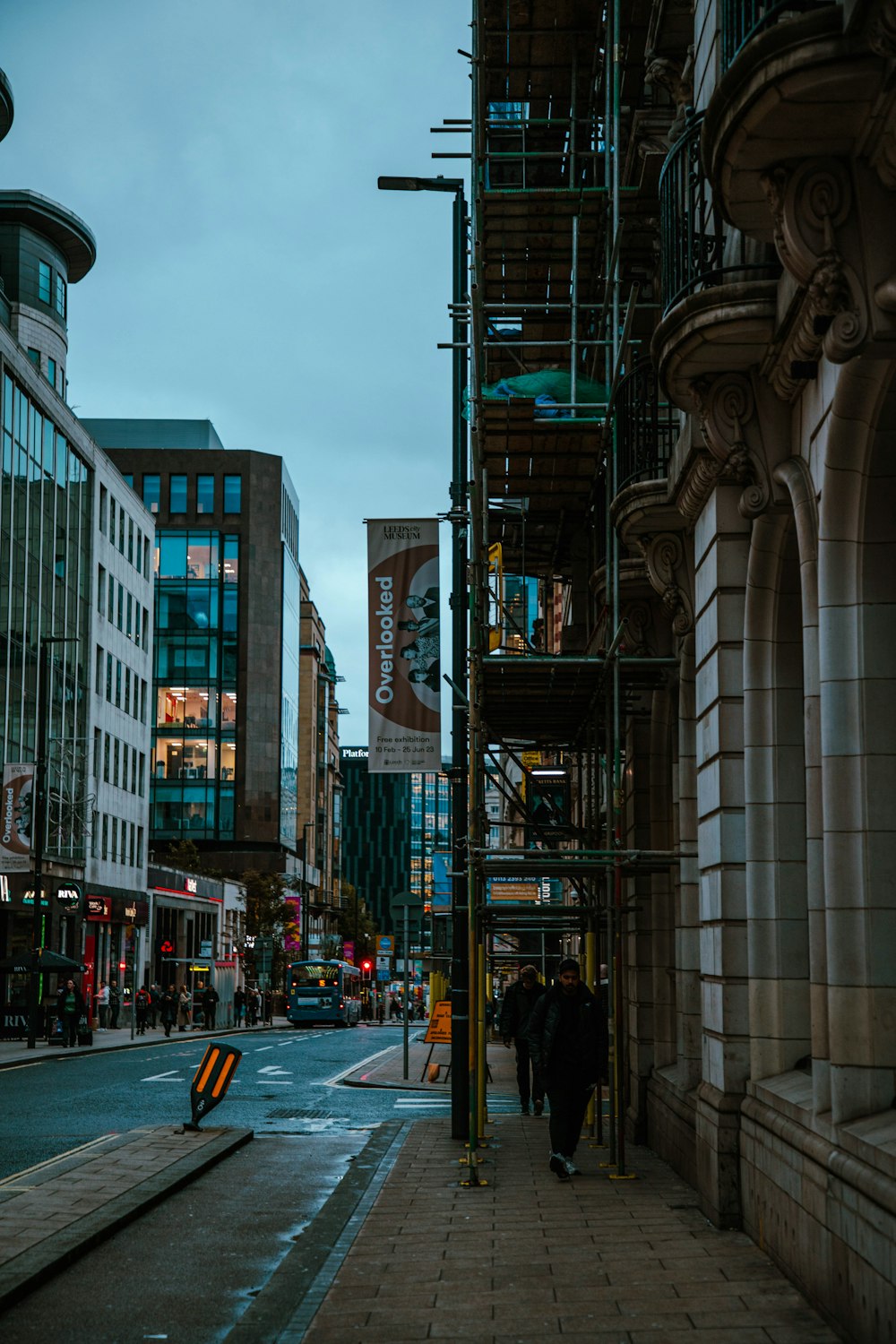 a couple of people walking down a street next to tall buildings