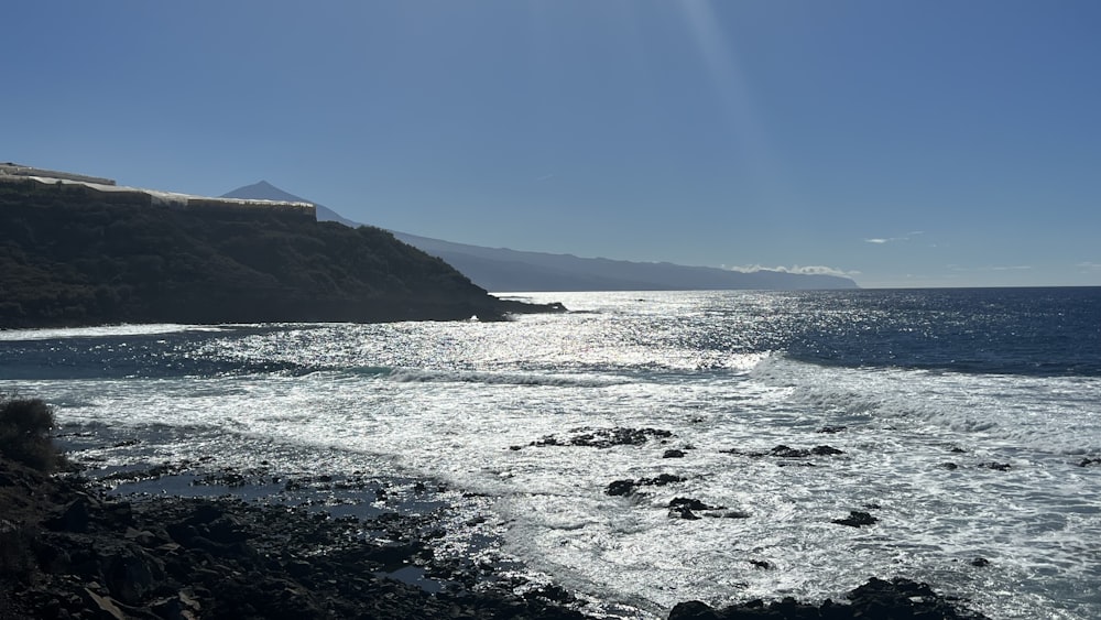 the sun shines on the ocean and rocky shore