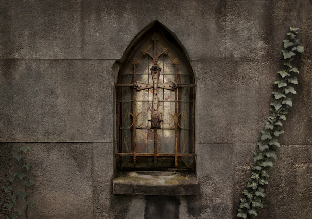 An old arched window framed by ivy on a rustic stone wall.