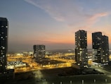 Wide-angle cityscape at dusk with glowing windows and soft evening hues.