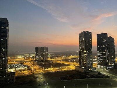 Wide-angle cityscape at dusk with glowing windows and soft evening hues.