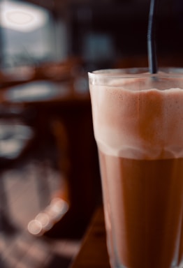 A vibrant photo of a barista pouring a creamy iced latte into a glass with ice, set against the stylish interior of Phnom Penh #1 Coffee.