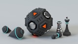 A futuristic and metallic black device with geometric shapes and orange accents is placed next to several chess pieces, including a king and a pawn. Two conical objects with a sleek, black finish and turquoise highlights are also present.