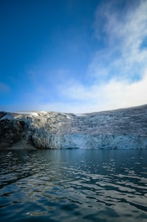 A serene scene of a glacier melting into a dark lake with electric blue accents in the water.