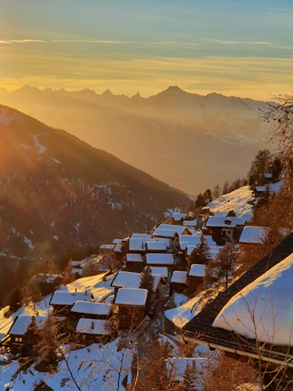 A cozy alpine cottage glowing warmly at dusk with the towering Adi Kailash peaks in the background.