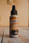A bottle of air freshener labeled 'Aroma's Antitabaco' placed on a wooden surface with a light beige background. The label also mentions eliminating strong odors for a longer time.
