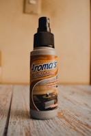 A bottle of air freshener labeled 'Aroma's Antitabaco' placed on a wooden surface with a light beige background. The label also mentions eliminating strong odors for a longer time.