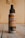 A bottle of air freshener labeled 'Aroma's Antitabaco' placed on a wooden surface with a light beige background. The label also mentions eliminating strong odors for a longer time.