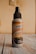 A bottle of air freshener labeled 'Aroma's Antitabaco' placed on a wooden surface with a light beige background. The label also mentions eliminating strong odors for a longer time.