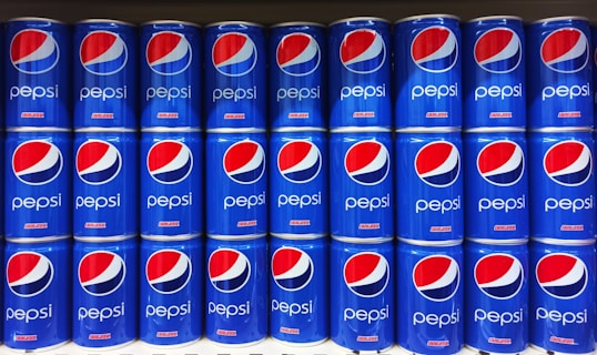 Rows of blue Pepsi cans are neatly stacked, displaying the distinctive red, white, and blue logo prominently on each can.